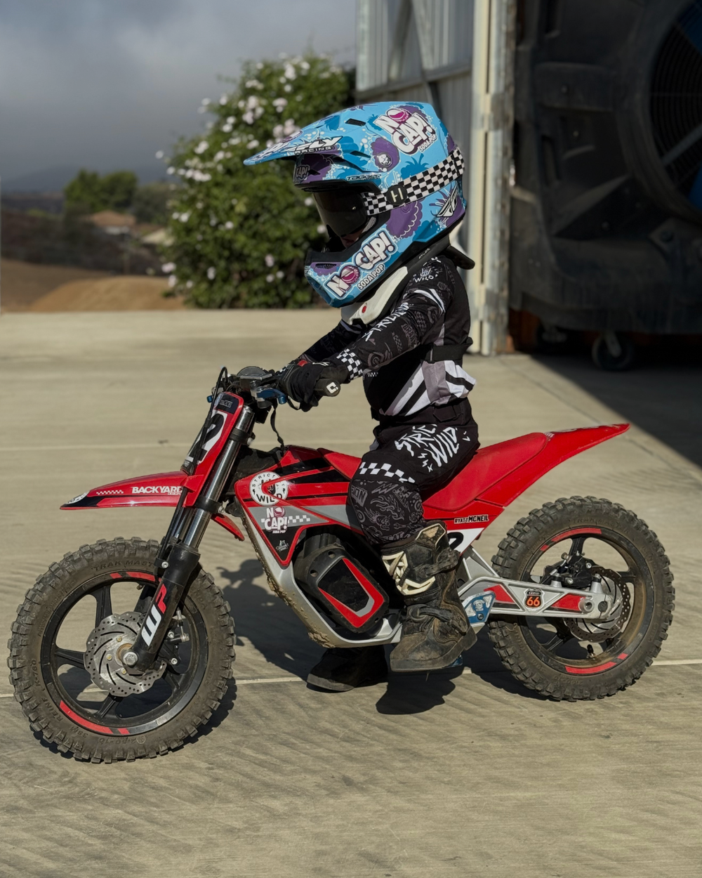 Child on a red dirt bike wearing a helmet with a checkered pattern.