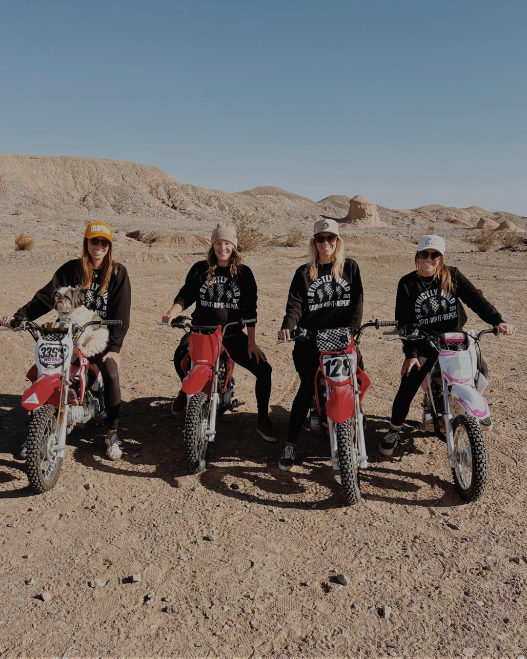 Four people on dirt bikes in a desert setting