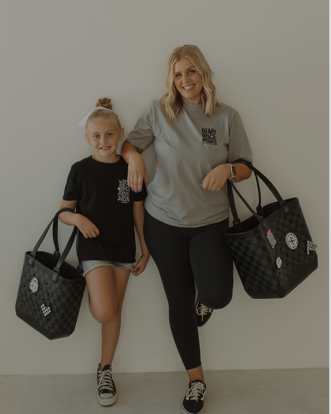Woman and young girl holding black bags against a plain background