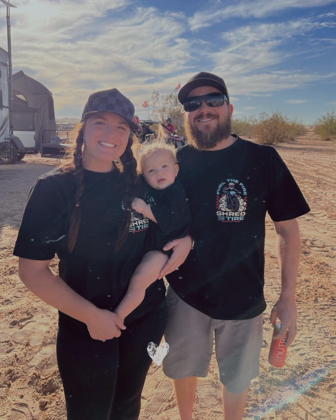 Family of three posing outdoors with a truck and trailer in the background