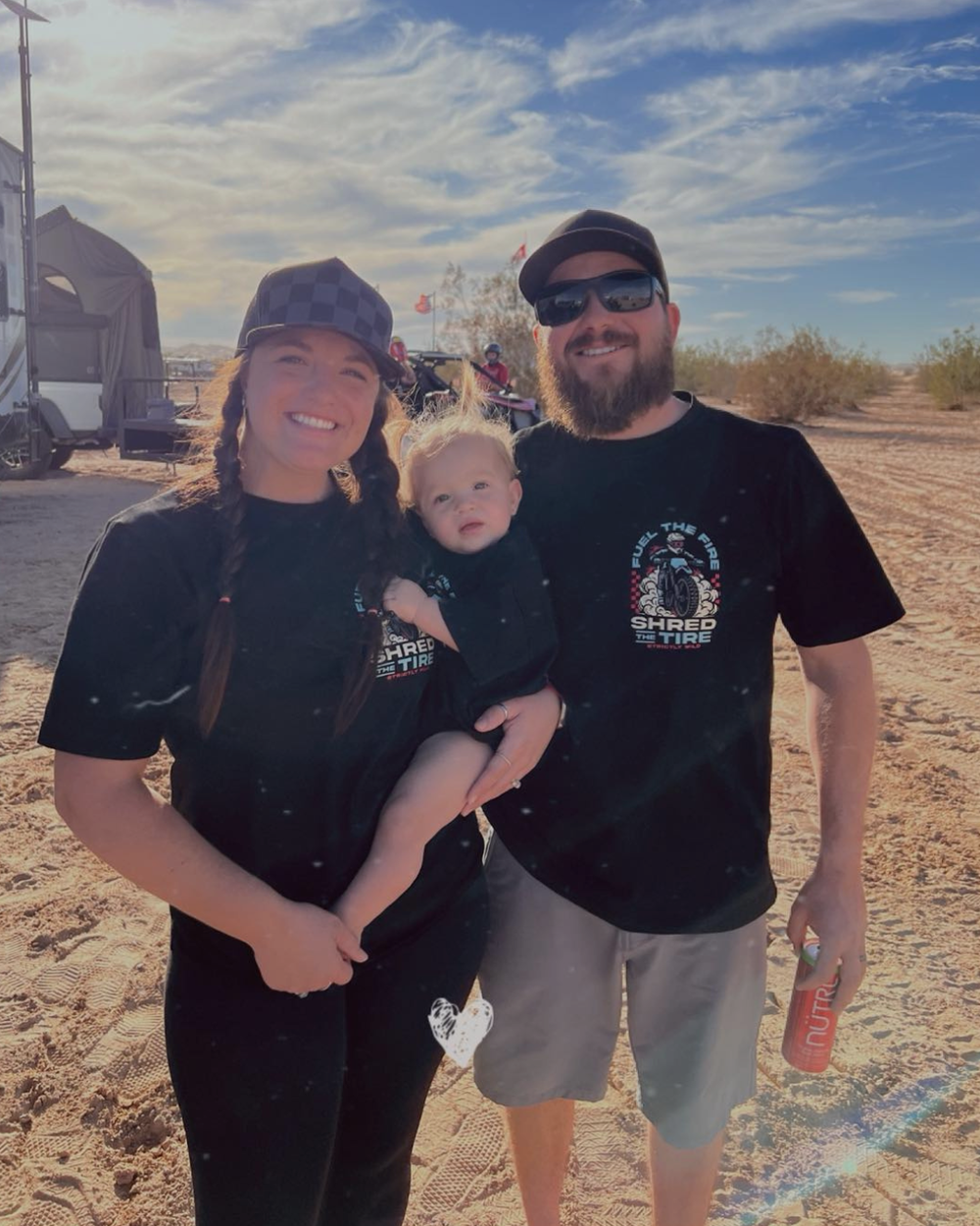 Family of three posing outdoors with a truck and trailer in the background