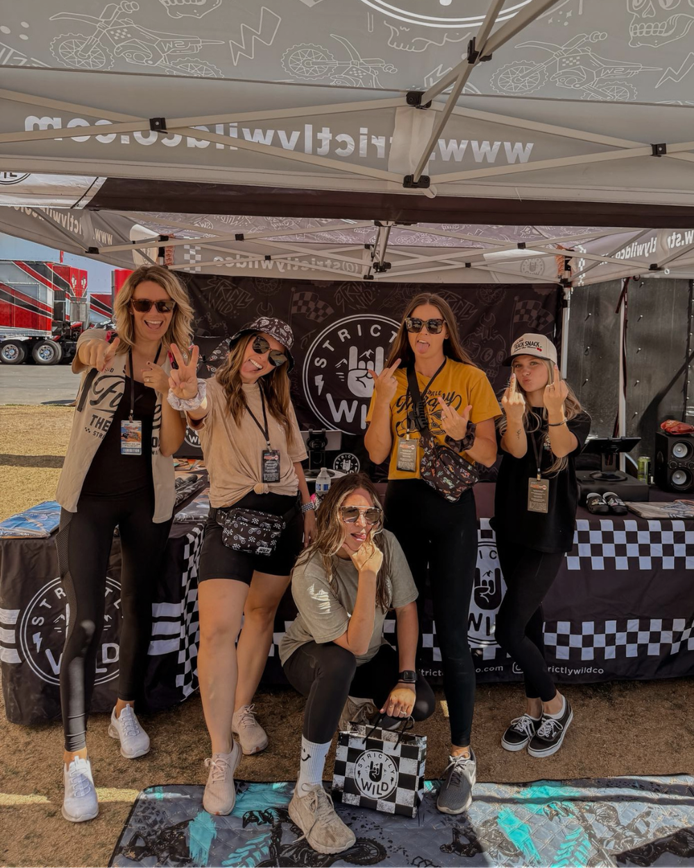Group of five women posing in front of a branded tent at an event.