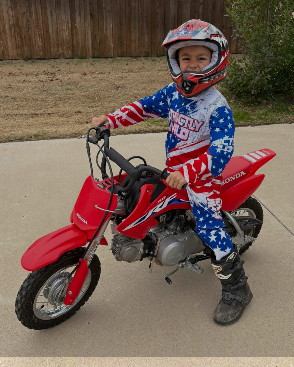 Child wearing a patriotic outfit and helmet on a red motorcycle.