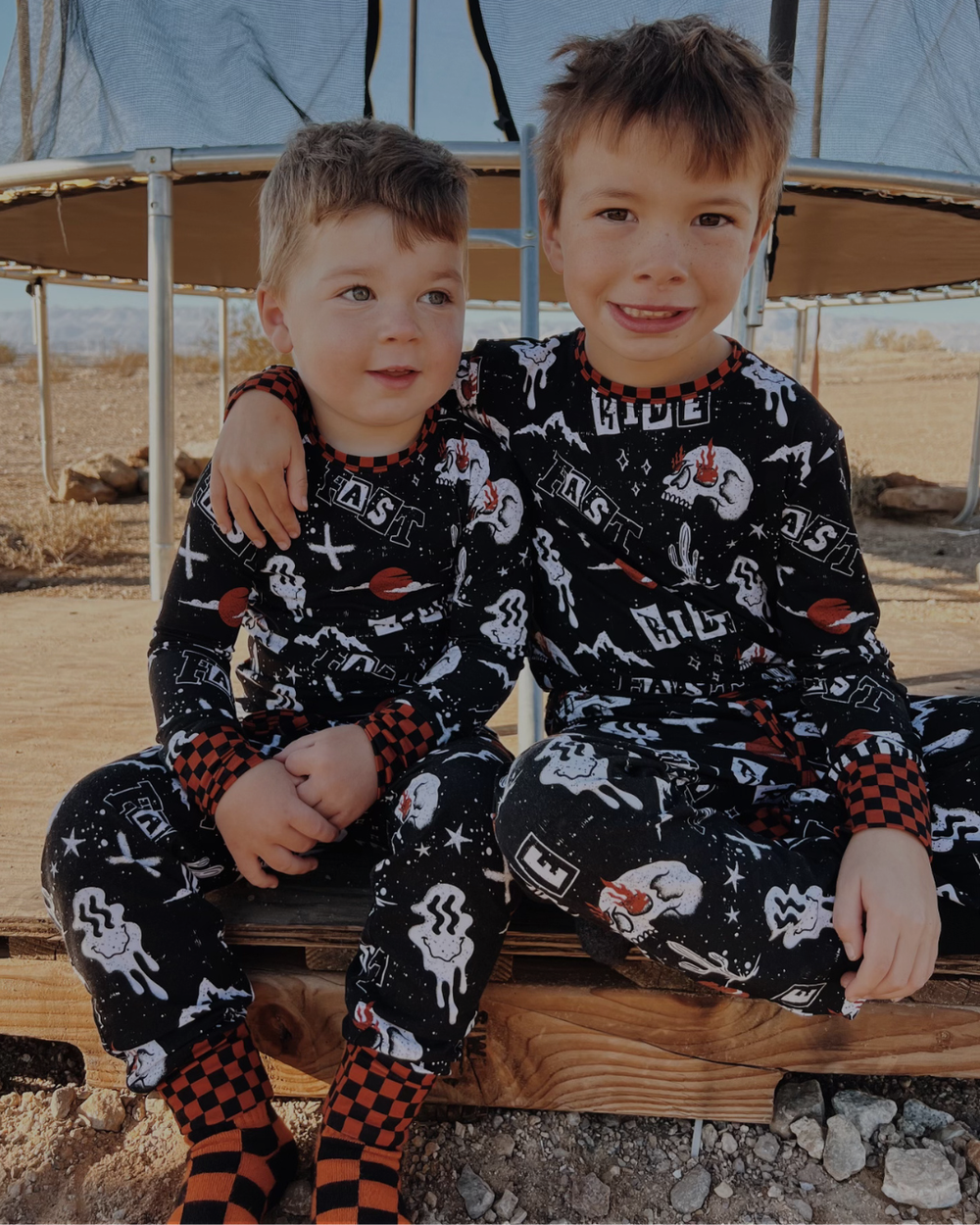 Two children wearing black pajamas with white patterns sitting on a wooden bench.