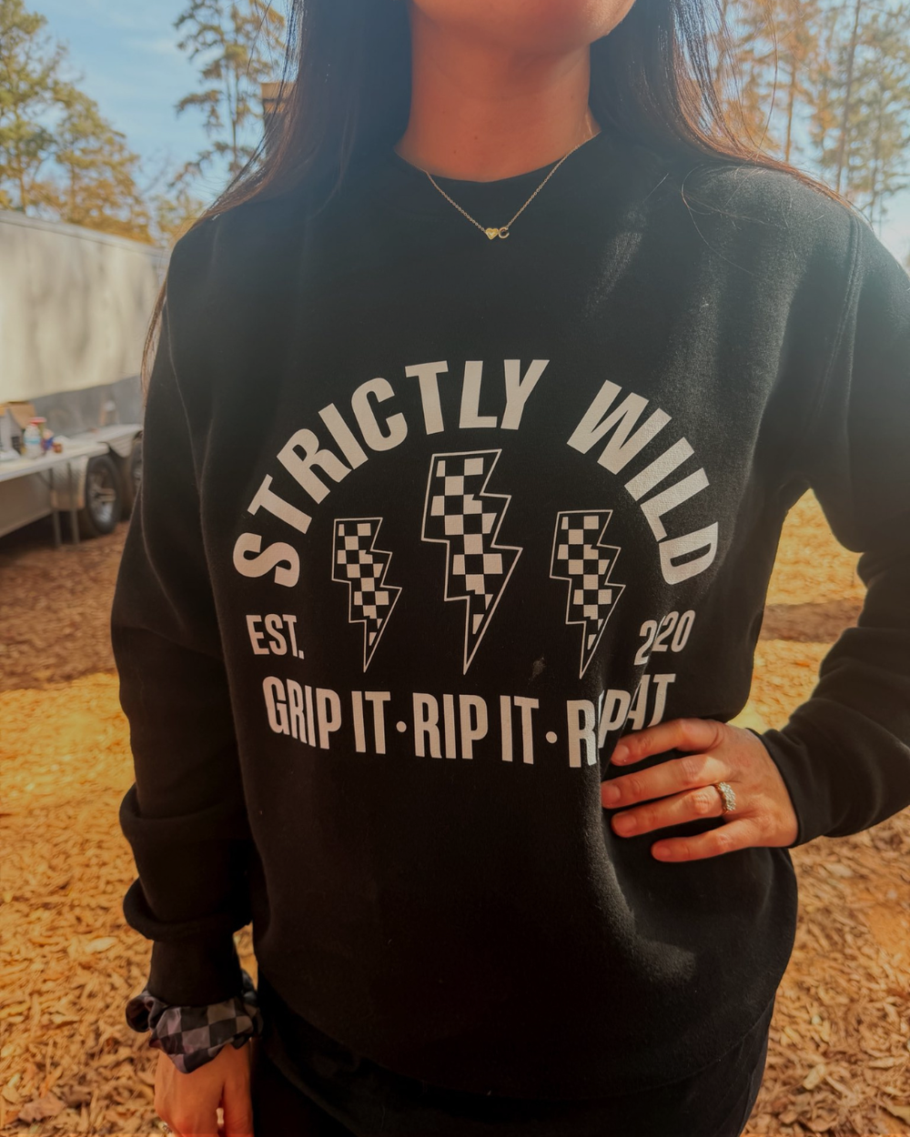 Person wearing a black sweatshirt with 'Strictly Wild' text and graphics outdoors.
